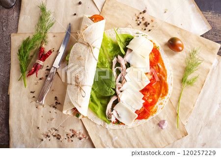 Sliced sandwich tortilla with tomatoes , salad , cream cheese and ham . 120257229