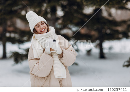 Happy smiling young woman with coffee hot drink cup enjoys winter weather at snowy winter park Happy smiling young woman with coffee hot drink cup enjoys winter weather at snowy winter park 120257411
