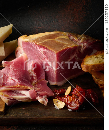 A piece of prosciutto, slices of ciabatta and cheese on a wooden board 120257510
