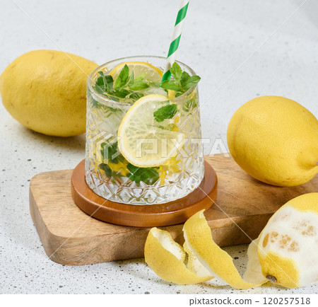 Transparent glass with lemon slices, mint leaves and ice cubes on white table Transparent glass with lemon slices, mint leaves and ice cubes on white table 120257518