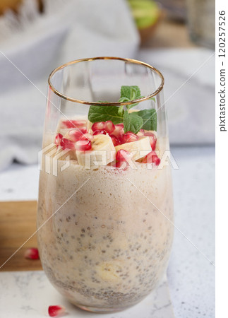 A glass of chia seeds and yogurt, with banana pieces and pomegranate seeds added to the dessert 120257526