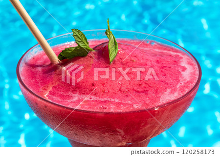 Chilled red drink with mint garnish by blue pool. Concept of summer refreshment and tropical relaxation Chilled red drink with mint garnish by blue pool. Concept of summer refreshment and tropical relaxation 120258173