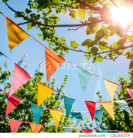 Colorful Triangle Flags Hanging Against Blue Sky and Green Leaves Colorful Triangle Flags Hanging Against Blue Sky and Green Leaves 120260254