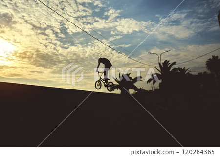Silhouette unrecognizable Young man doing ramp jump stunt on bmx bicycle on sunset. Silhouette unrecognizable Young man doing ramp jump stunt on bmx bicycle on sunset. 120264365
