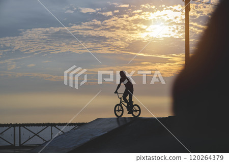 Silhouette unrecognizable Young man doing ramp jump stunt on bmx bicycle on sunset. Silhouette unrecognizable Young man doing ramp jump stunt on bmx bicycle on sunset. 120264379