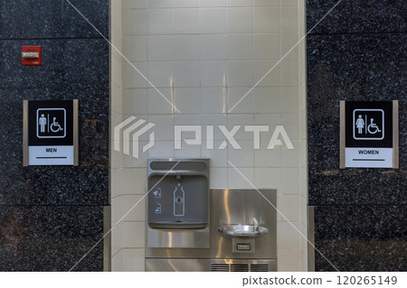 Entrance to public restroom features clear signs for men, women facilities, including accessible options for individuals with disabilities nearby water fountain. Entrance to public restroom features clear signs for men, women facilities, including accessible options for individuals with disabilities nearby water fountain. 120265149