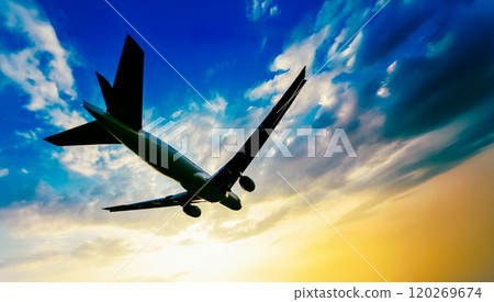 A sunset-tinted plane flies through the sky 120269674