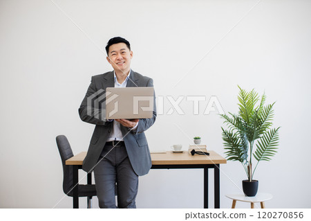 Confident businessman with laptop in modern office environment 120270856