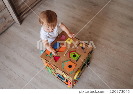 Child plays with busy board. Educational toys for children, wooden game panel Child plays with busy board. Educational toys for children, wooden game panel 120273045