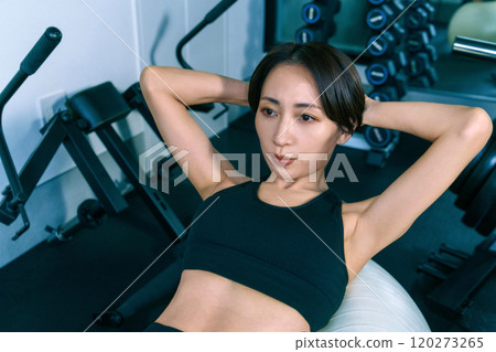 Woman doing abdominal exercises using balance ball at gym Woman doing abdominal exercises using balance ball at gym 120273265