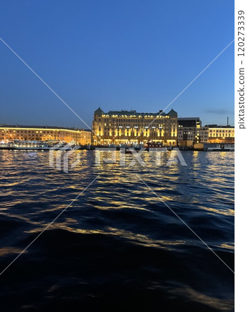 Illuminated Waterfront Building Reflecting on Dark Waters 120273339
