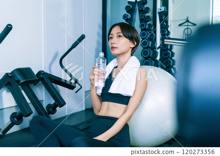 A woman taking a break leaning against a balance ball at the gym 120273356