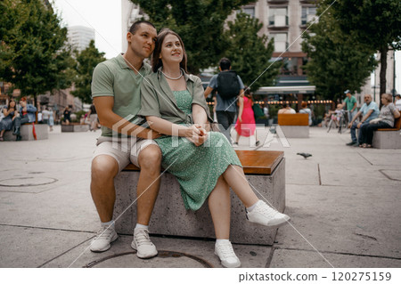 Couple enjoying a casual conversation on a bench outdoors in a city. A couple chats and smiles together while seated on a bench in city Warsaw. Poland. Couple in love visiting Warsaw. 120275159