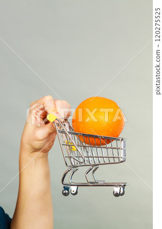 Woman holding shopping cart with orange inside Woman holding shopping cart with orange inside 120275525