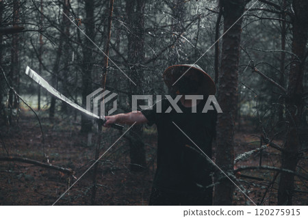 A man trains with a katana. A swordsman wearing a conical Asian hat holds a katana in the forest while it rains. The man practices his sword technique in a dark atmospheric environment. 120275915