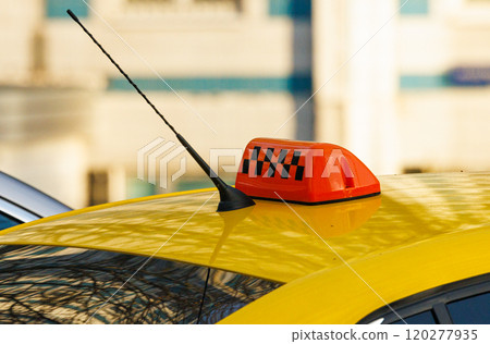 Bright yellow taxi cab with an orange rooftop light signaling pick up in a busy urban street during the day 120277935