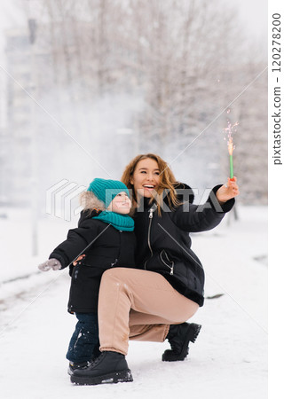 Smiling mom and little son are standing in the snow, with holding sparkler Smiling mom and little son are standing in the snow, with holding sparkler 120278200