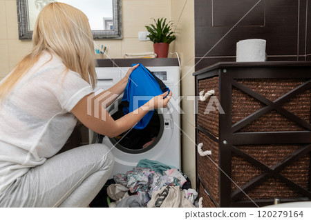 A woman is thoughtfully loading her laundry into the washing machine in a contemporary laundry room 120279164