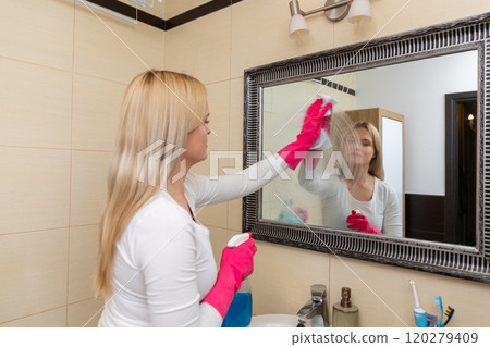 A woman diligently cleaning her bathroom mirror using a spray for a clear reflection 120279409