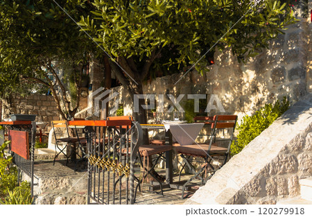 An inviting outdoor dining spot with rustic charm, set among stone walls and dappled sunlight, perfect for a leisurely, peaceful meal in nature. 120279918