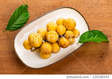 Top view of a bunch of ripe Long kong in brown ceramic tray with dark edge on wooden table. Top view of a bunch of ripe Long kong in brown ceramic tray with dark edge on wooden table. 120280547
