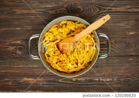 Sauteed yellow peppers being prepared in a frying pan with wooden spatula on wooden countertop 120280820