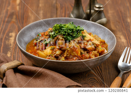 Hearty vegetable curry served in a rustic bowl on a wooden table with fresh herbs on top 120280841