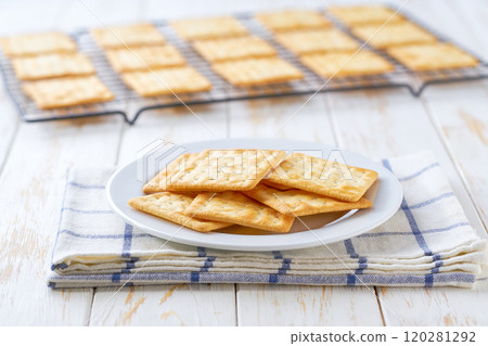 Freshly baked wheat water crackers cooling on a black wire rack, with in a light kitchen table, selective focus. 120281292