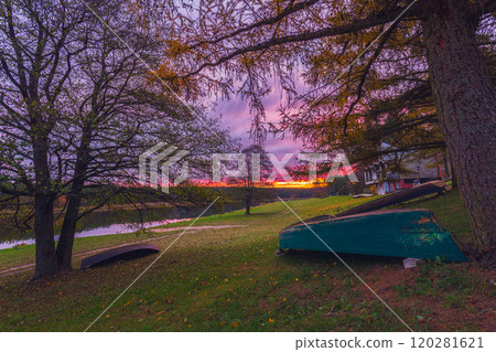Experience the Serene Sunset by the Water, Surrounded by Colorful Autumn Leaves and a Peaceful Boat Experience the Serene Sunset by the Water, Surrounded by Colorful Autumn Leaves and a Peaceful Boat 120281621