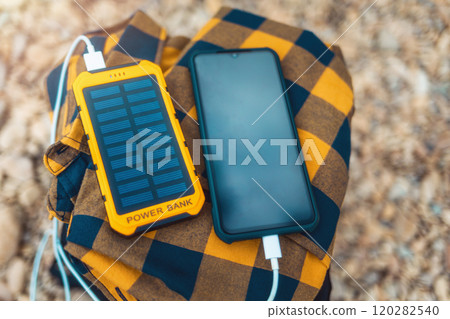 Power bank charges the smartphone via a USB cable. Top view, close-up. Pebble on the background. Copy space. Concept of modern gadgets 120282540