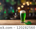 Glass of green festive beer and clover shamrock on wooden table. Blurred background with lights. St. Patrick Day Festival Banner. Template with copy space and montage. Generative Ai 120282560