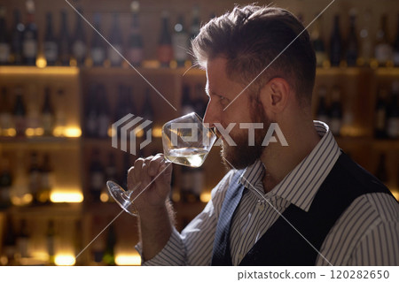 High angle shot of brutal Caucasian man in smart clothes inhaling perfect scent of botanical white wine High angle shot of brutal Caucasian man in smart clothes inhaling perfect scent of botanical white wine 120282650