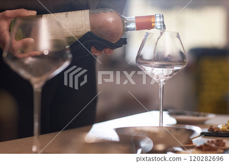 Medium close up of unrecognizable female sommelier holding bottle of white wine and pouring into prefect crystal glass Medium close up of unrecognizable female sommelier holding bottle of white wine and pouring into prefect crystal glass 120282696