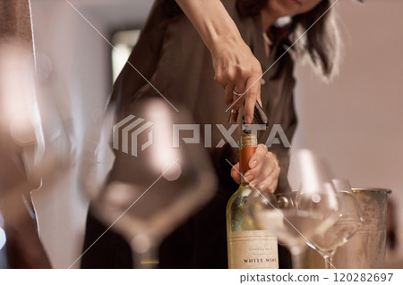 Medium close up of unrecognizable women opening wine bottle with metal corkscrew 120282697
