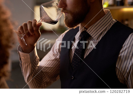 Medium close up of unrecognizable man in smart clothes holding crystal glass with red wine, he expertizing aroma 120282719