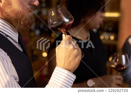 Medium close up of unrecognizable male sommeliers holding crystal glass of wine in hand while scenting aroma 120282720