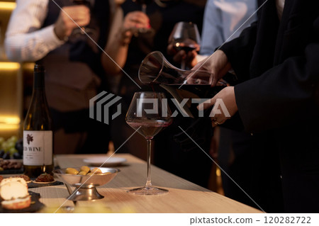 Medium close up of presentation limited edition wine, unrecognizable female hand holding pitcher full with wine while pouring glass 120282722