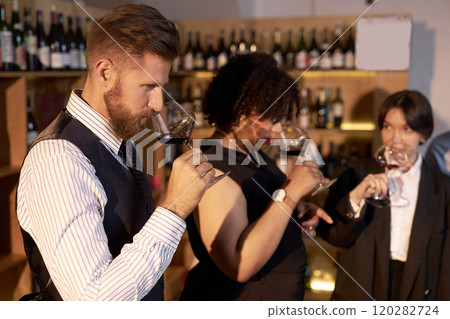 High angle shot of mixed race sommeliers scenting aromatic wine while having glasses in hands High angle shot of mixed race sommeliers scenting aromatic wine while having glasses in hands 120282724
