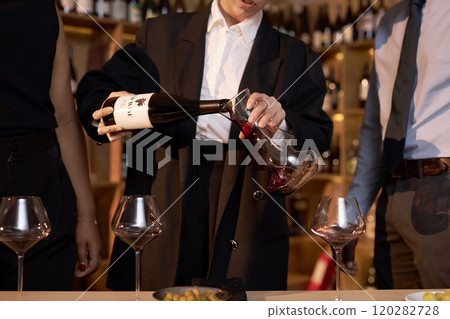 Medium close up of unrecognizable female sommelier pouring wine into crystal glass pitcher during degustation in wine cellar Medium close up of unrecognizable female sommelier pouring wine into crystal glass pitcher during degustation in wine cellar 120282728