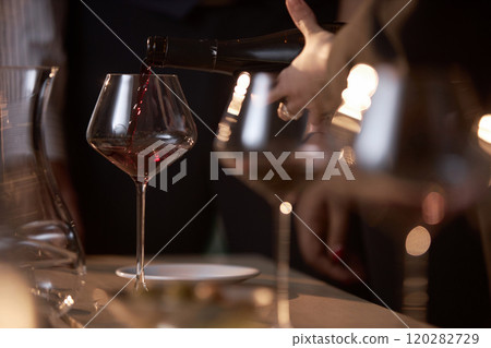 Medium close up of polished crystal glasses with red wine, unrecognizable woman pouring aromatic beverage into wineglass Medium close up of polished crystal glasses with red wine, unrecognizable woman pouring aromatic beverage into wineglass 120282729