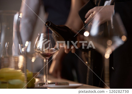 Medium close up of unrecognizable woman pouring aromatic and semi-sweet red wine into polished crystal glass on tasting table Medium close up of unrecognizable woman pouring aromatic and semi-sweet red wine into polished crystal glass on tasting table 120282730
