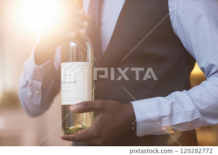 Medium close up of golden sunrays illumining crystal bottle with sime-sweet white wine in unrecognizable African American sommelier 120282772