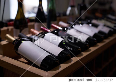 Medium close up of dimly lit bottles with aged red wine on wooden table during presentation Medium close up of dimly lit bottles with aged red wine on wooden table during presentation 120282842