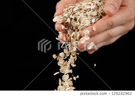 Hands pouring uncooked raw oatmeal on a black background. 120282962