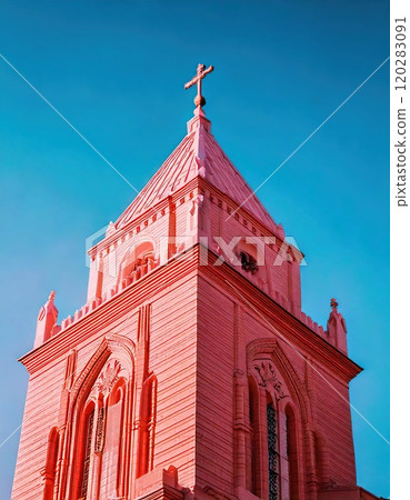 A church tower rises prominently against a clear blue sky, showcasing intricate architectural details. 120283091