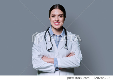 Portrait of young confident smiling woman doctor with crossed arms on gray background Portrait of young confident smiling woman doctor with crossed arms on gray background 120283298