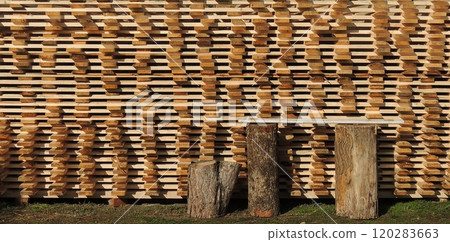bench made of two tree stumps and a board standing next to a textured wall made of end grain planed boards in natural sunlight, background texture on the theme of forest processing 120283663