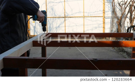 man drilling holes in wooden frame during construction of outbuilding in yard, working with building frame using hand tool in village 120283664