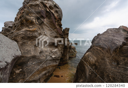 Rocky shore with ocean waves and dark stones under a cloudy sky, emphasizing the natural beauty of the coast 120284340