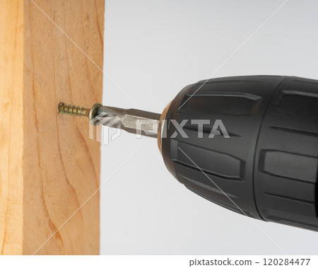 A screwdriver confidently screws a metal screw into a wooden board. 120284477